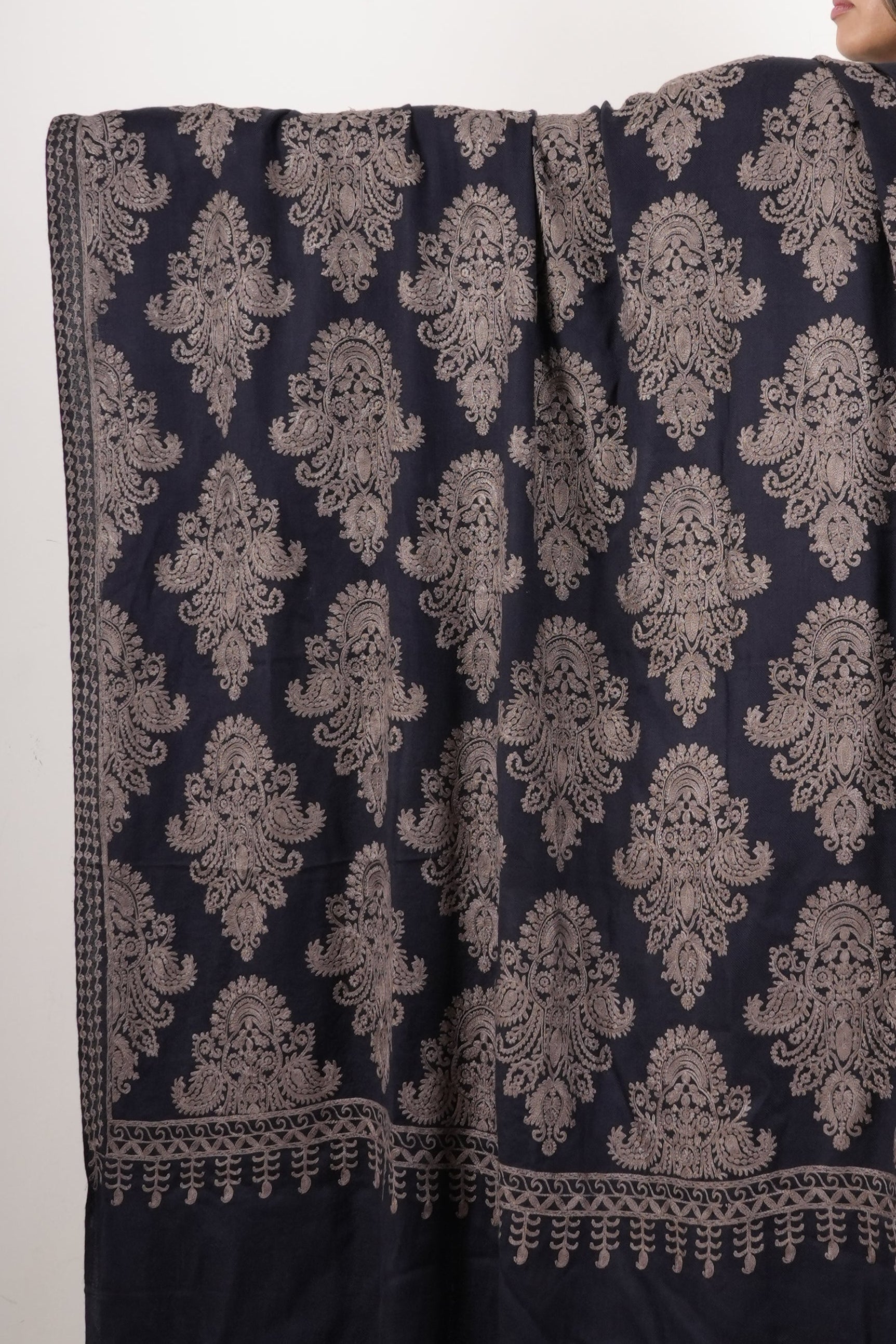 Woman holding a large dark blue and gold patterned fabric on a plain background